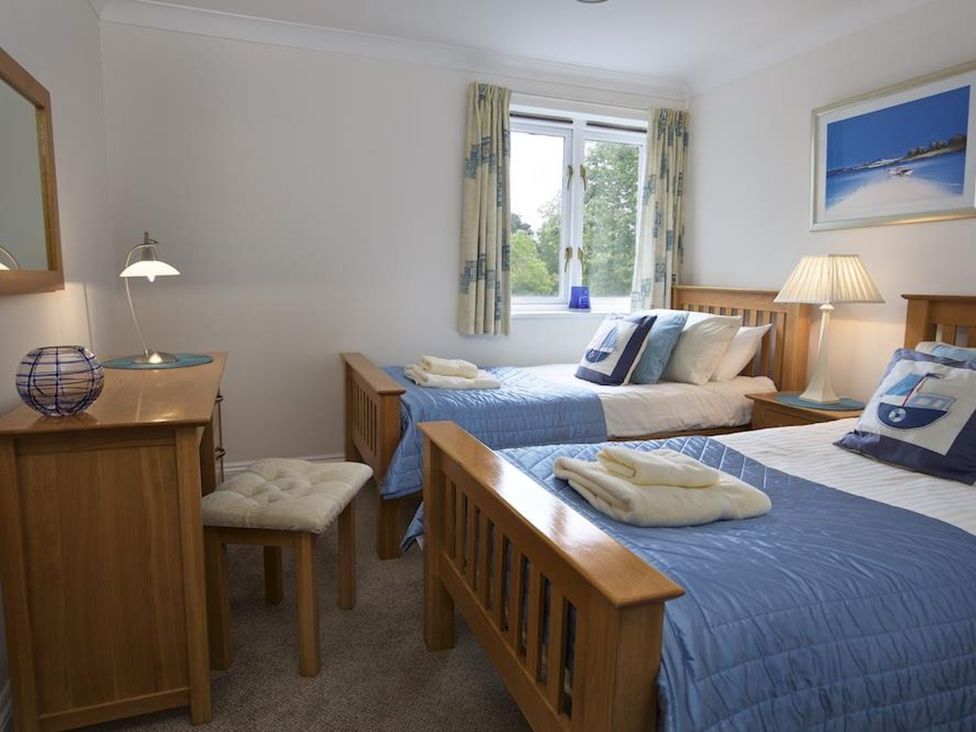 A bedroom with two single wooden beds blue bedding bedside table with lamp and dressing table at 10 Dartmouth House in Dartmouth
