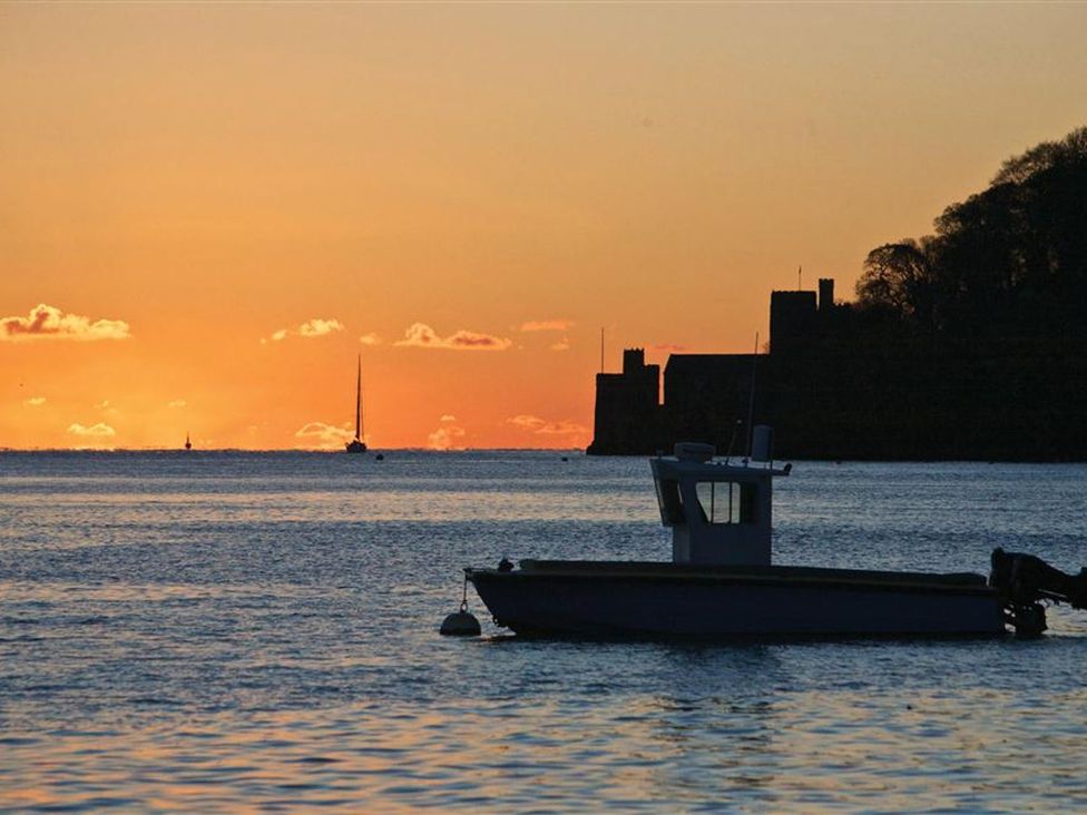 A boat on water during sunset with a castle silhouette and a sailboat in the distance at 10 Dartmouth House in Dartmouth