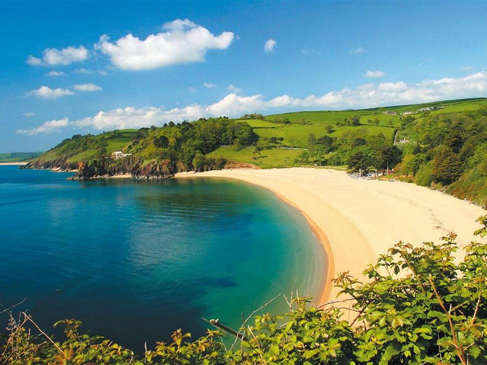A curved sandy beach with calm blue water and green hills in the background at 10 Dartmouth House in Dartmouth