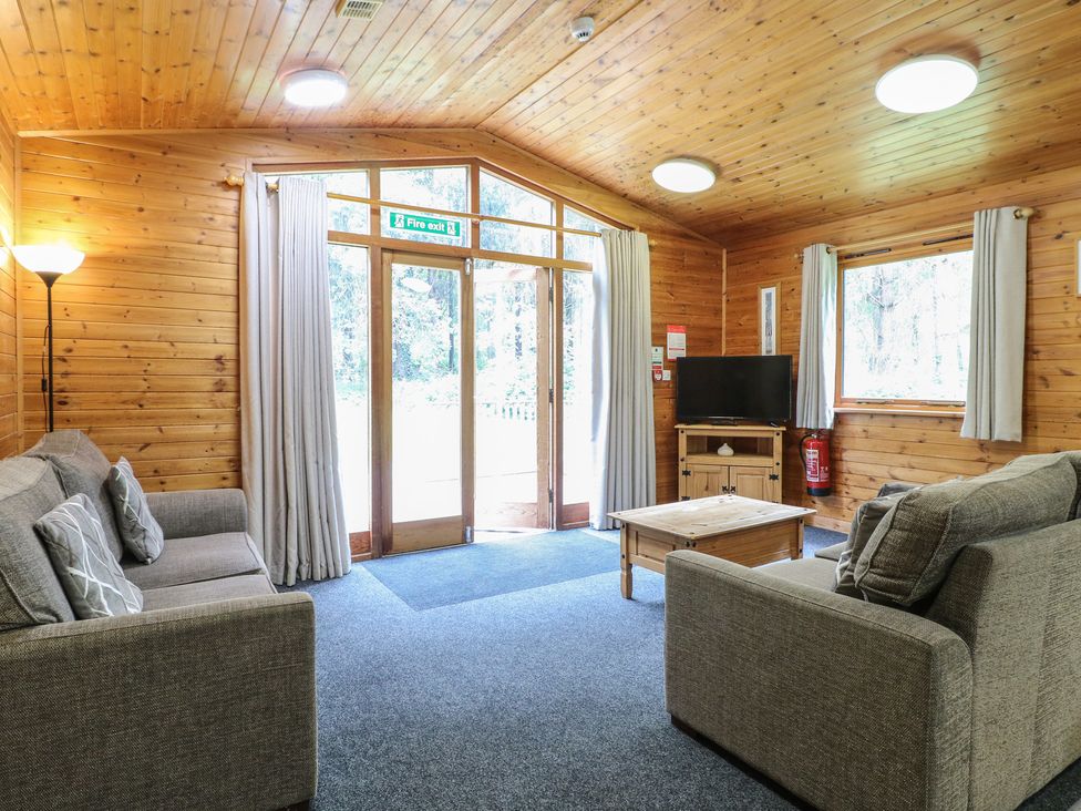A living room with two gray sofas a wooden coffee table a standing lamp a TV on a wooden stand and large windows at Sycamore Lodge in Rosliston