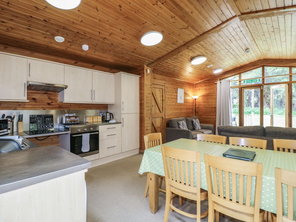 A kitchen and dining area with wooden chairs a green tablecloth and gray sofas at Sycamore Lodge in Rosliston