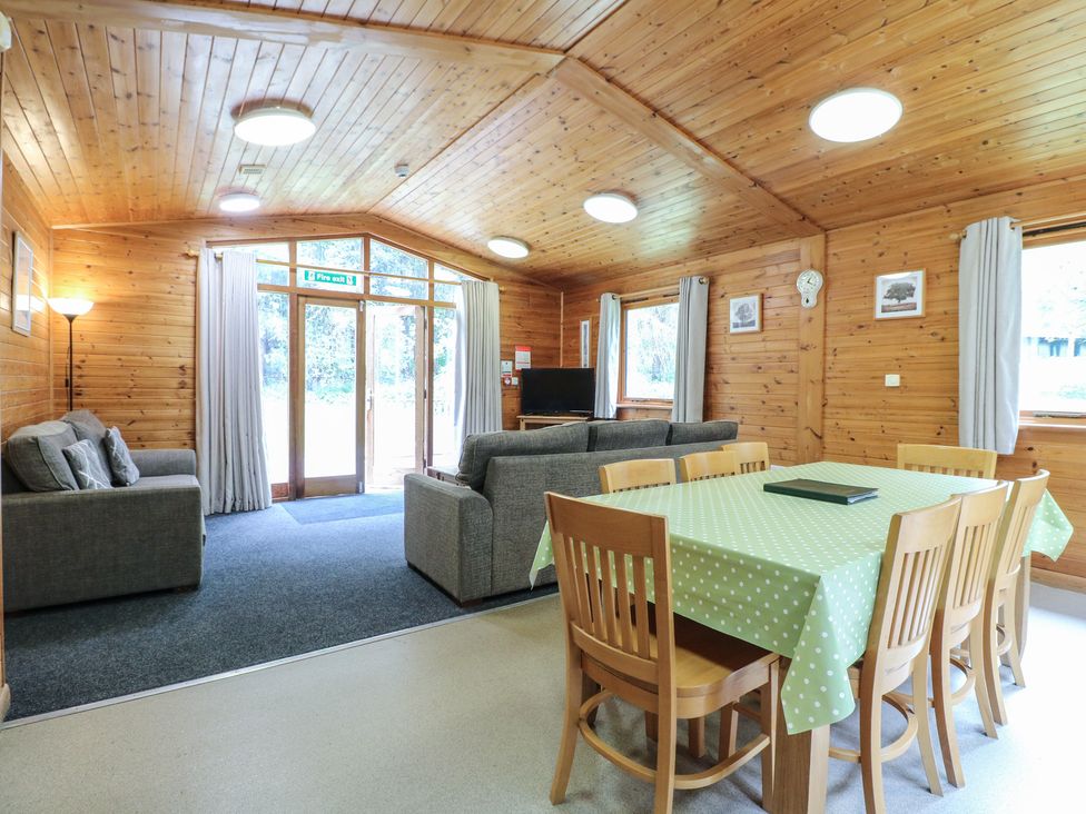 A wooden room with a dining table covered with a green polka dot tablecloth and chairs a sitting area with sofas and a television at Sycamore Lodge in Rosliston