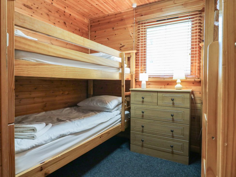 A small bedroom with wooden bunk beds and a chest of drawers under a window with blinds at Sycamore Lodge in Rosliston