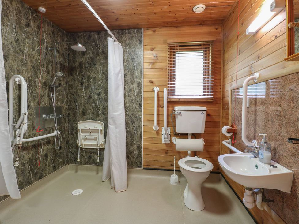 A bathroom with a shower area a toilet a sink and wooden walls at Sycamore Lodge in Rosliston
