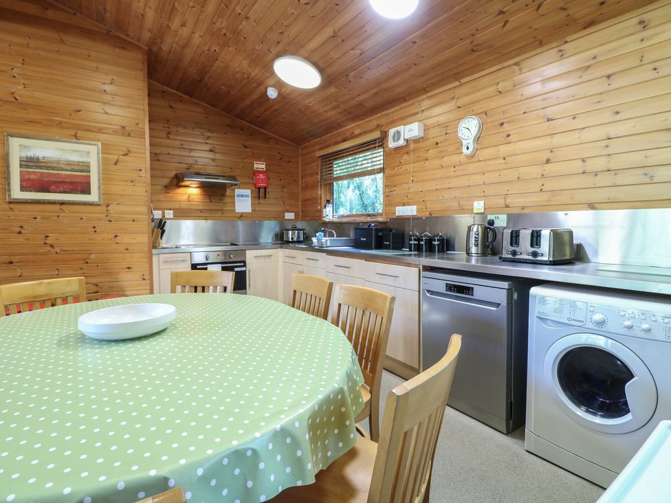 A kitchen with wooden walls a round table with a green polka dot tablecloth chairs and appliances including a washing machine and dishwasher at Cedar Lodge in Rosliston