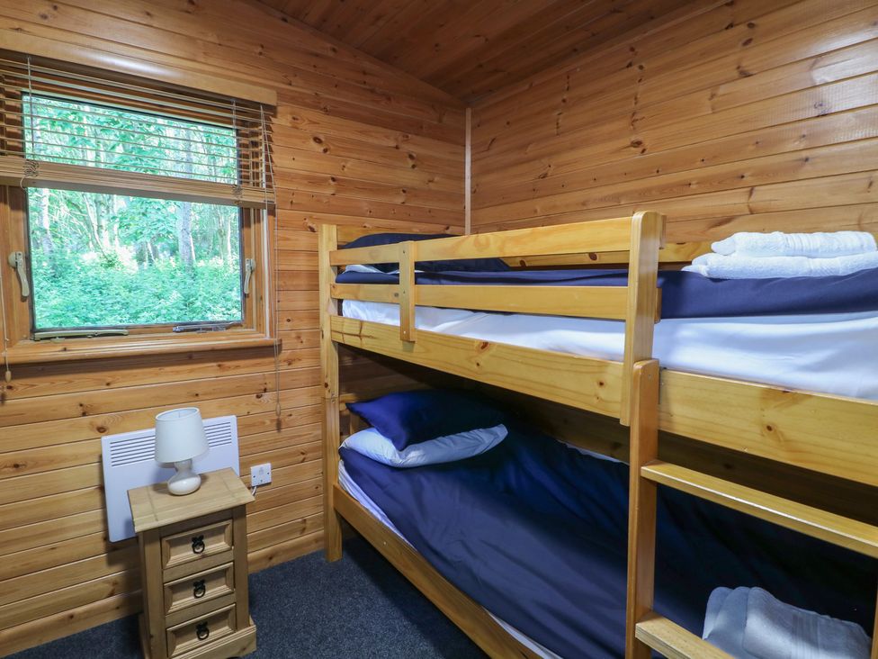 A wooden bedroom with bunk beds beside a window and a small wooden bedside table with a lamp at Cedar Lodge in Rosliston