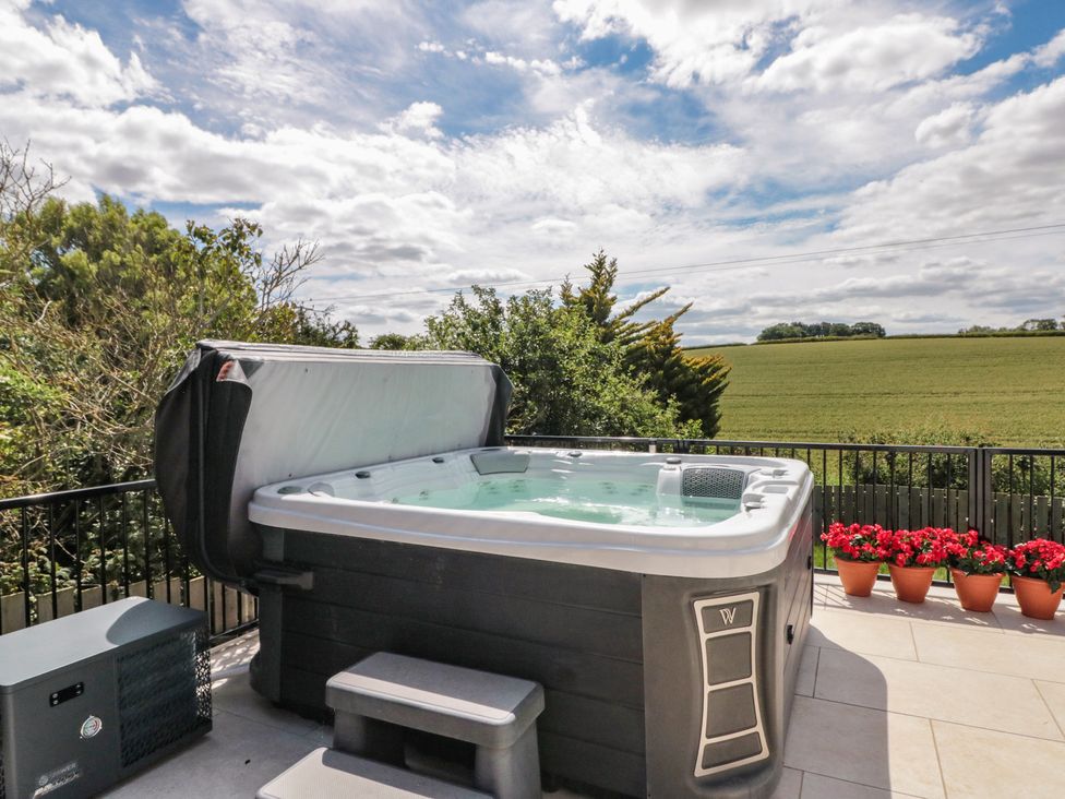 A hot tub on a patio overlooking a green landscape at Puffin Lodge in Hunmanby