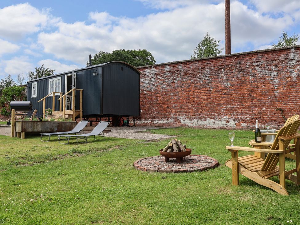 An outdoor space with a hut, fire pit, and chairs at Shepherd's Hut in Wrexham