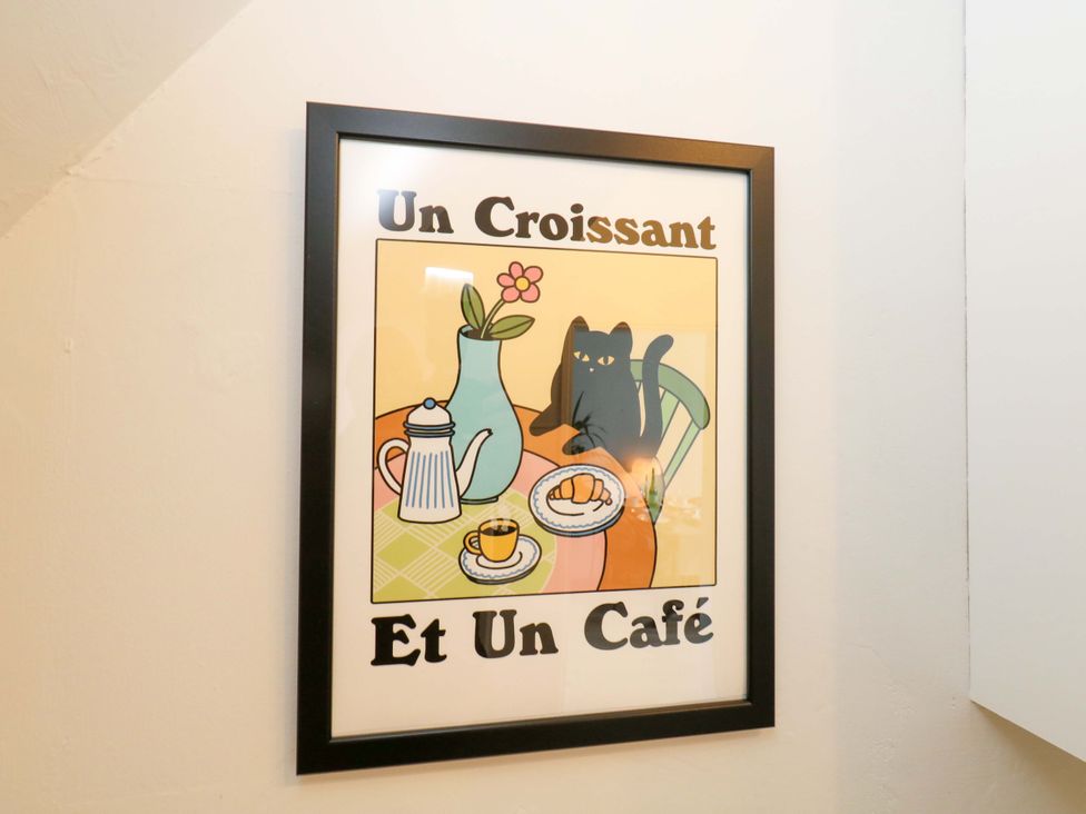 A framed artwork featuring a cat, coffee, and croissant in the dining room at Seagull & Chips in Weymouth