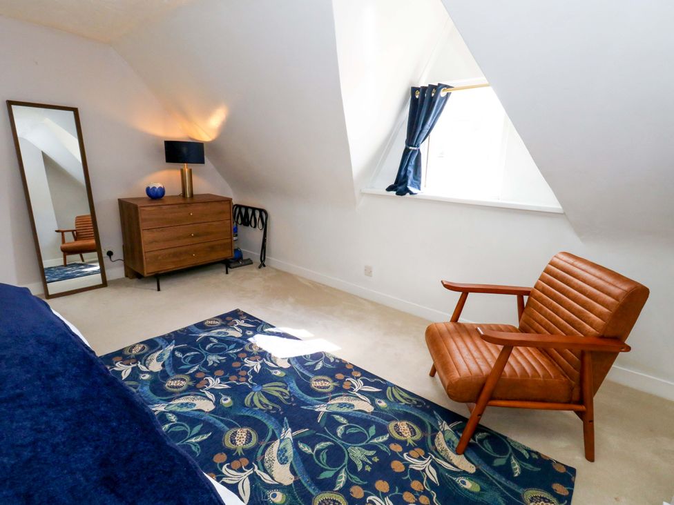A bedroom with a mirror, lamp, dresser, and a chair at Seagull & Chips in Weymouth