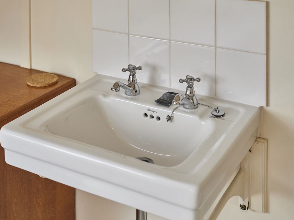 A sink with faucets and wall tiles at Beachside Cottage in Sandsend