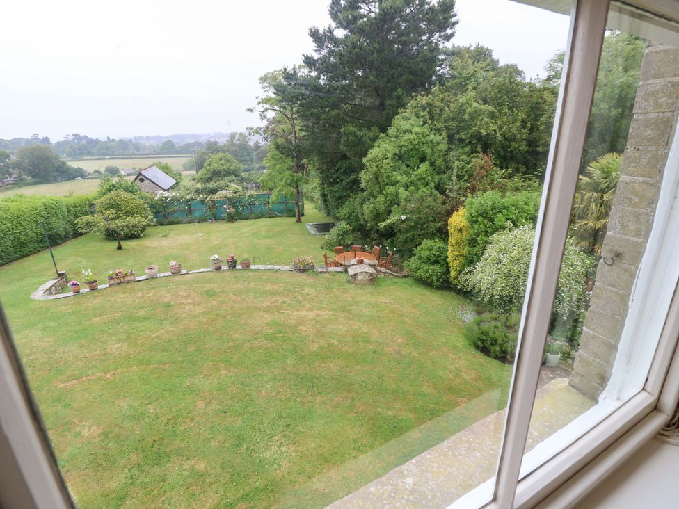 A garden view with trees and furniture seen from a window at Woodlands in Freshwater