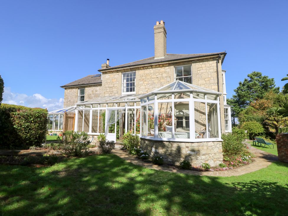 An outdoor view of a house with a conservatory and garden at Woodlands in Freshwater