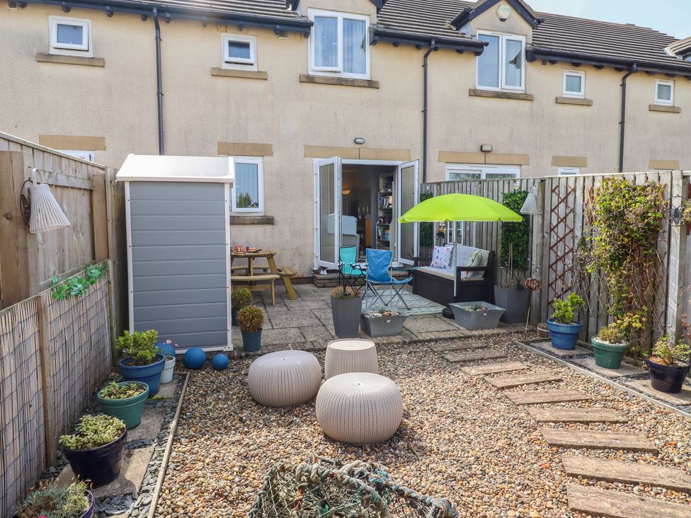 A garden with a shed, table, chairs, and flower pots at Tidal Watch in Seahouses
