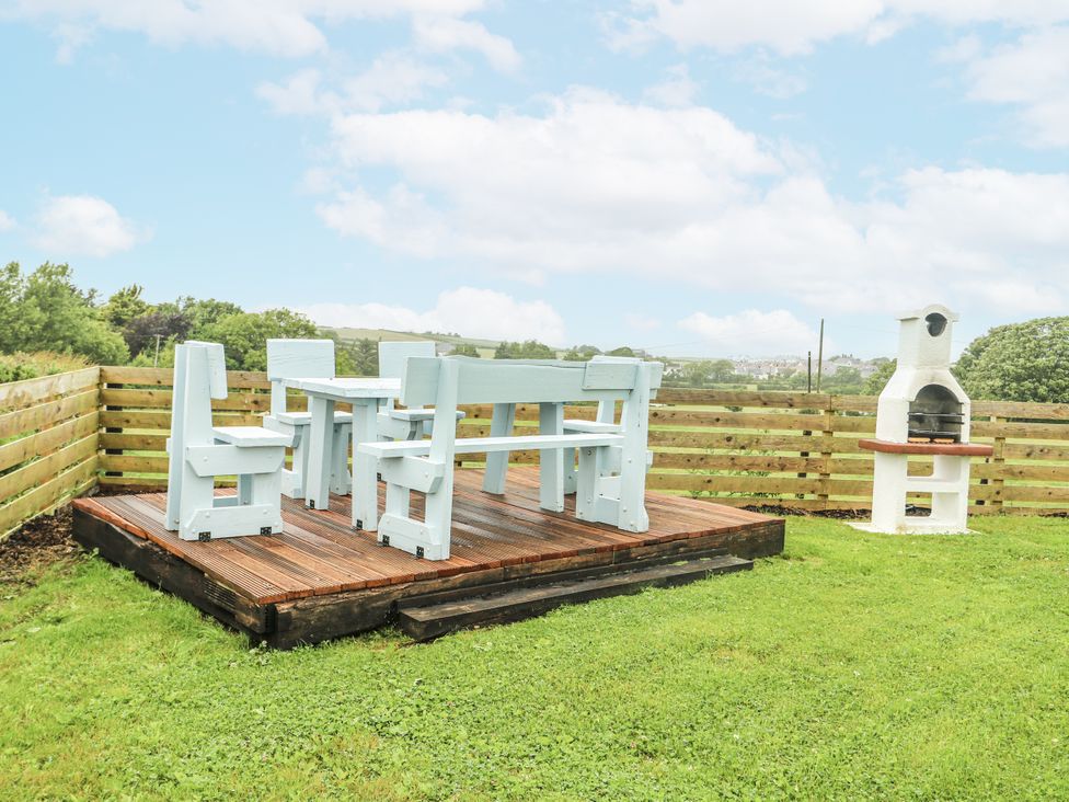 A garden with a wooden deck, table, chairs and barbecue at The Old Cornmill in Cemaes Bay