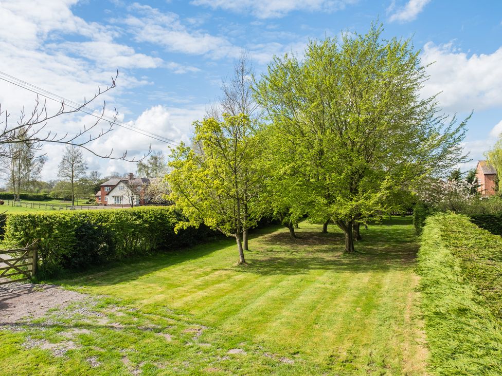 A garden with trees and a house in the background at Hall O'Coole in Broomhall near Wrenbury