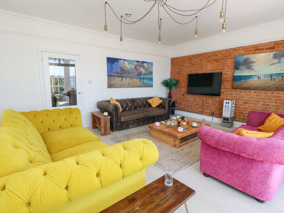 A living room with a yellow sofa, brown sofa, and pink sofa at The Beach Condo in Weymouth