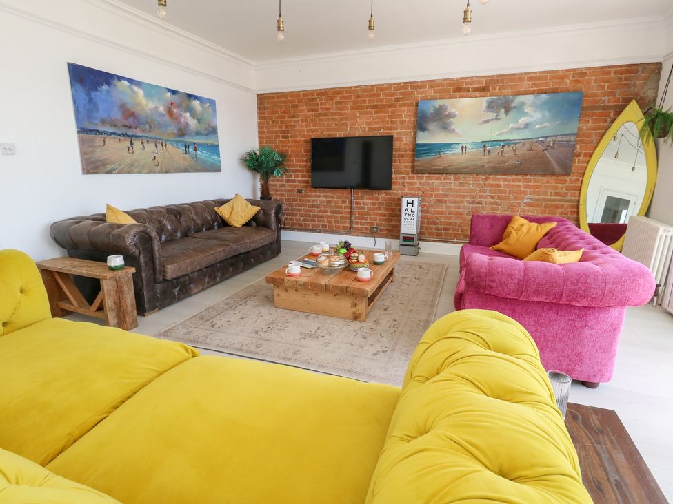A living room with a yellow and pink sofa and paintings on the wall at The Beach Condo in Weymouth