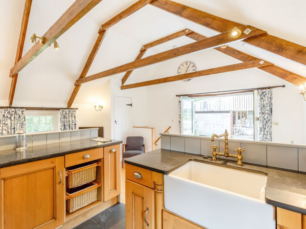 A kitchen with wooden cabinets a farmhouse sink and exposed wooden beams at The Loft in Bodrean near Truro