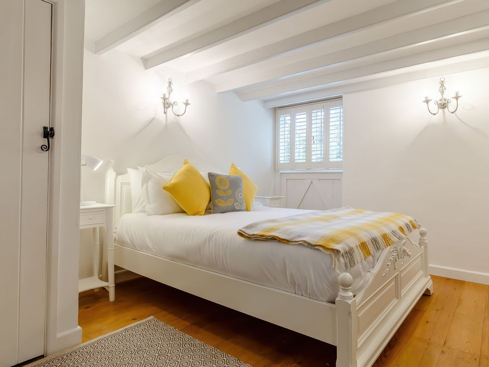 A bedroom with a white bed with yellow and gray pillows a yellow checkered blanket wooden floor white walls and a window with shutters at The Loft in Bodrean near Truro