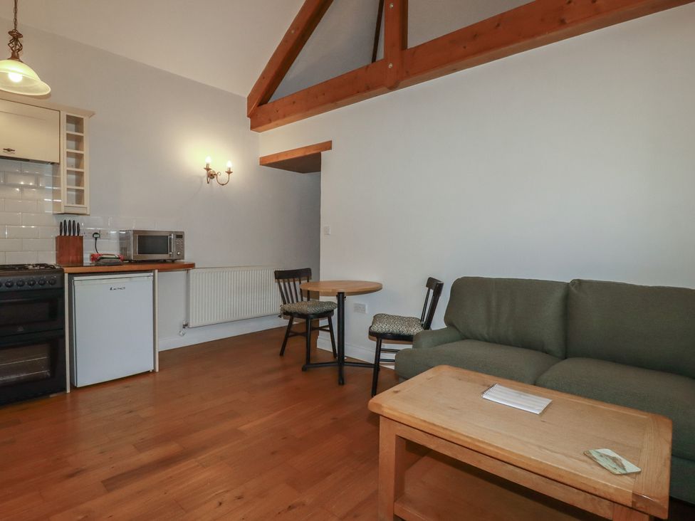 A small kitchen and living area with a stove fridge microwave table chairs sofa and wooden coffee table at The Copper House in Bodrean near Truro