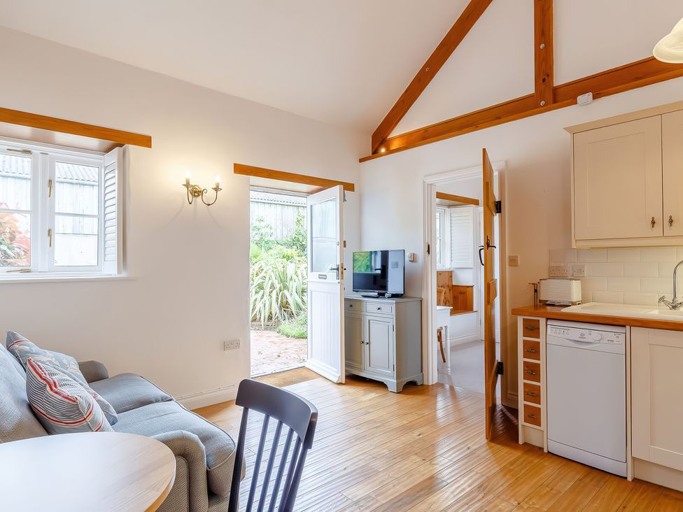 A kitchen and living area with wooden floor wooden beams a sofa a round table a dishwasher and a TV at The Copper House in Bodrean near Truro