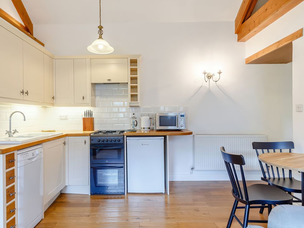 A kitchen with white cabinets wooden countertops a stove dishwasher microwave kettle and a dining table with black chairs at The Copper House in Bodrean near Truro