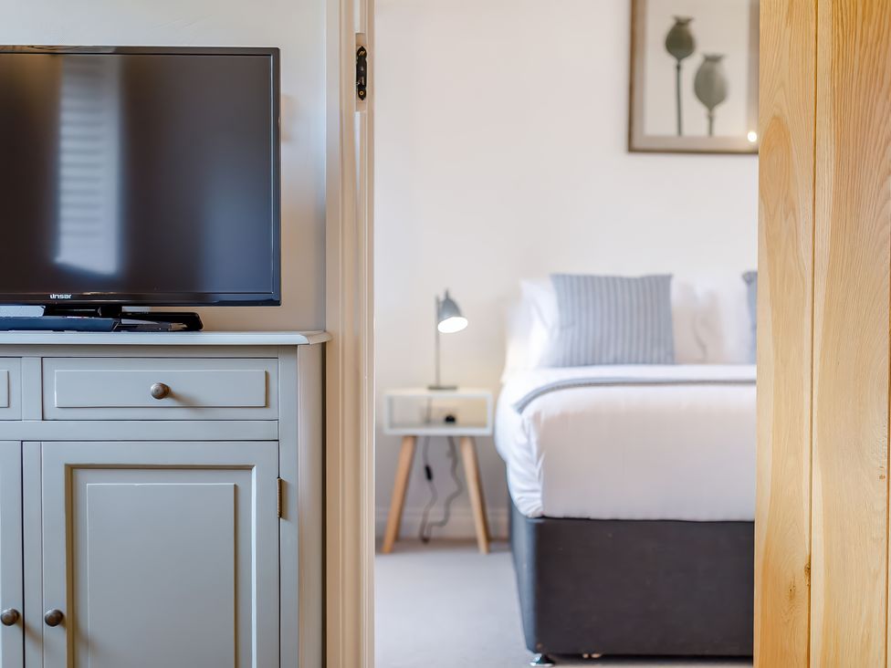 A television on a cabinet next to a bedroom with a bed bedside table and lamp at The Copper House in Bodrean near Truro