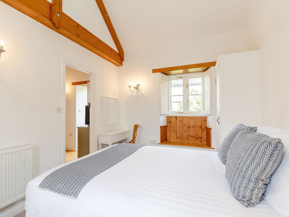 A bedroom with a bed pillows a window seat with wooden paneling a desk chair and exposed wooden ceiling beams at The Copper House Bodrean near Truro