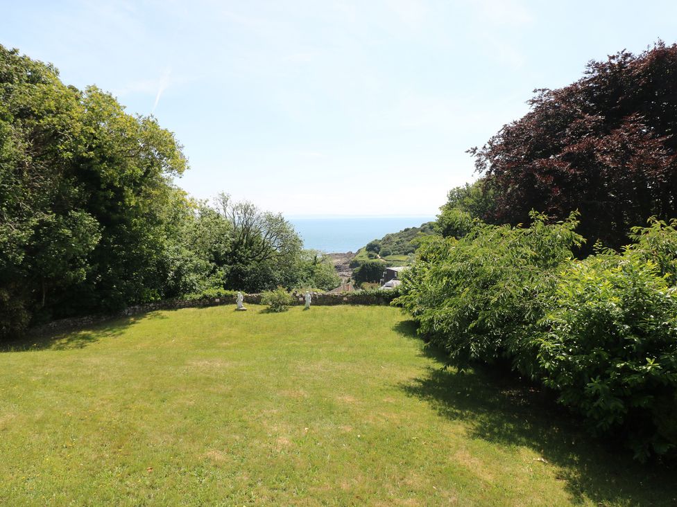 A garden with grass, trees, and a view of the sea at Whiteshell in Langland near Mumbles