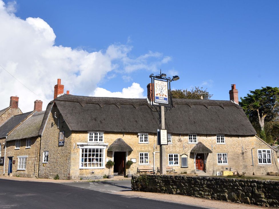 A building with a thatched roof and sign at 2 Bredy Cottages in Burton Bradstock