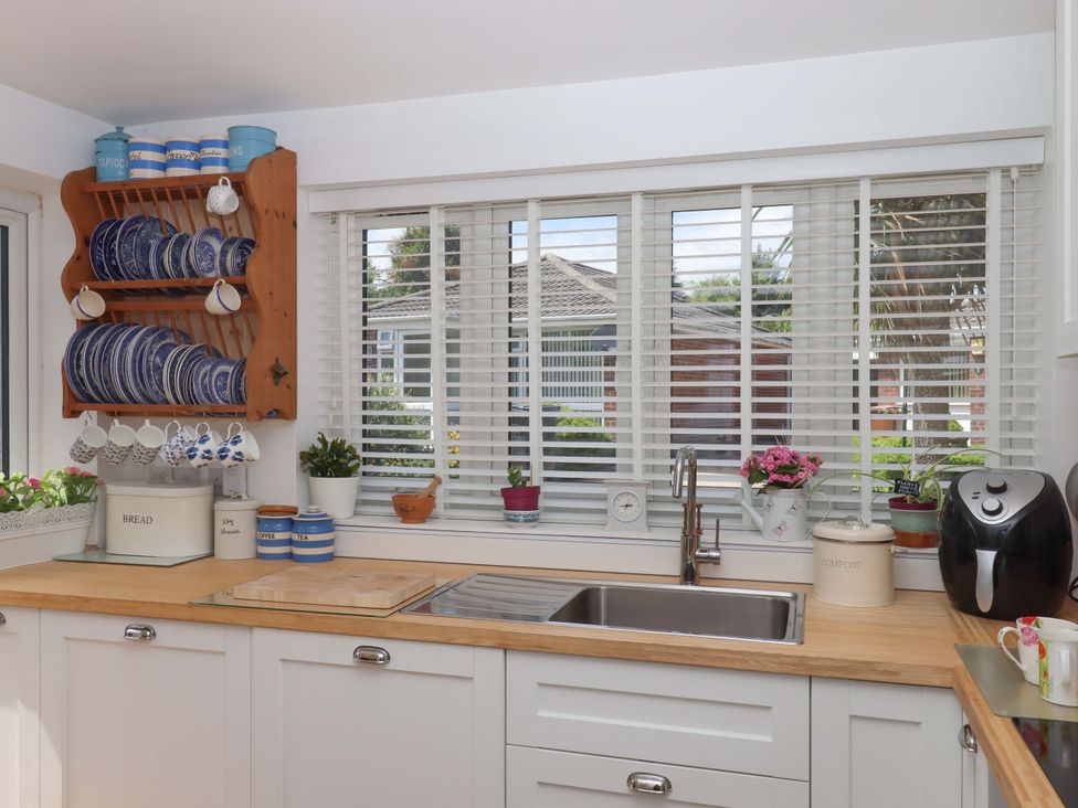 A kitchen with a sink and shelf holding plates and cups at Rowan in Brixham