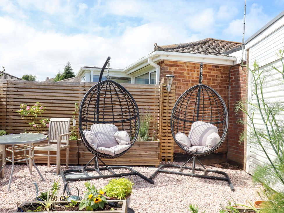 A garden with hanging chairs and a table at Rowan in Brixham