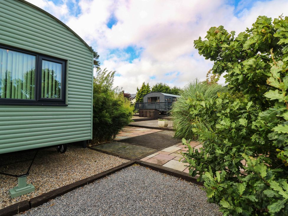 An outdoor area with a green cabin and wooden deck at Ava Lodge West Mains near Haggerston
