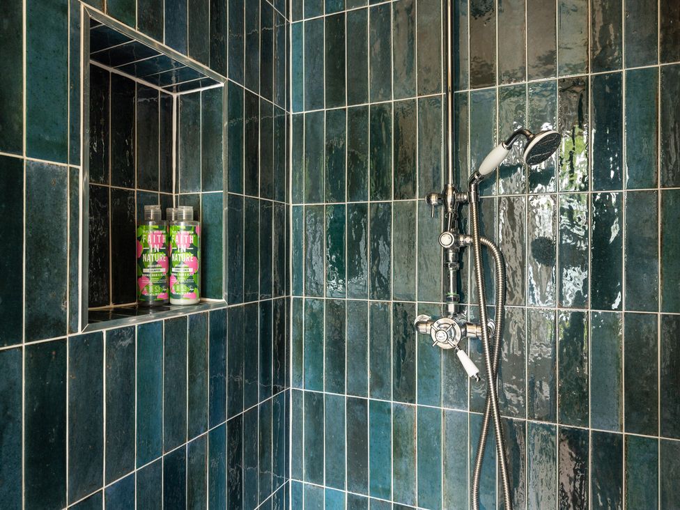 A shower with green tiles and shampoo bottles at The Old Vicarage Merriott