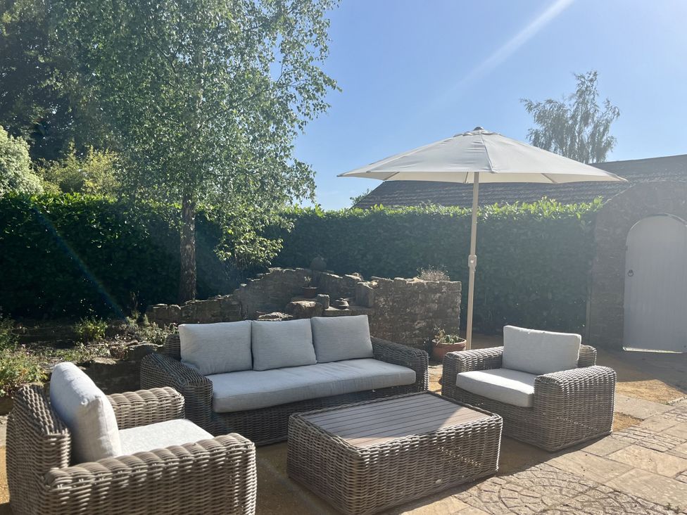 A seating area with a sofa and table under a parasol at The Old Vicarage in Merriott