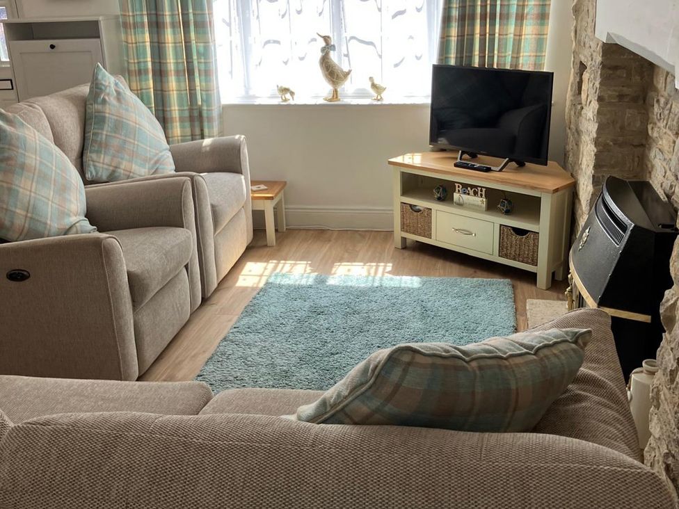 A living room with a sofa, armchair, and television at Claire Cottage