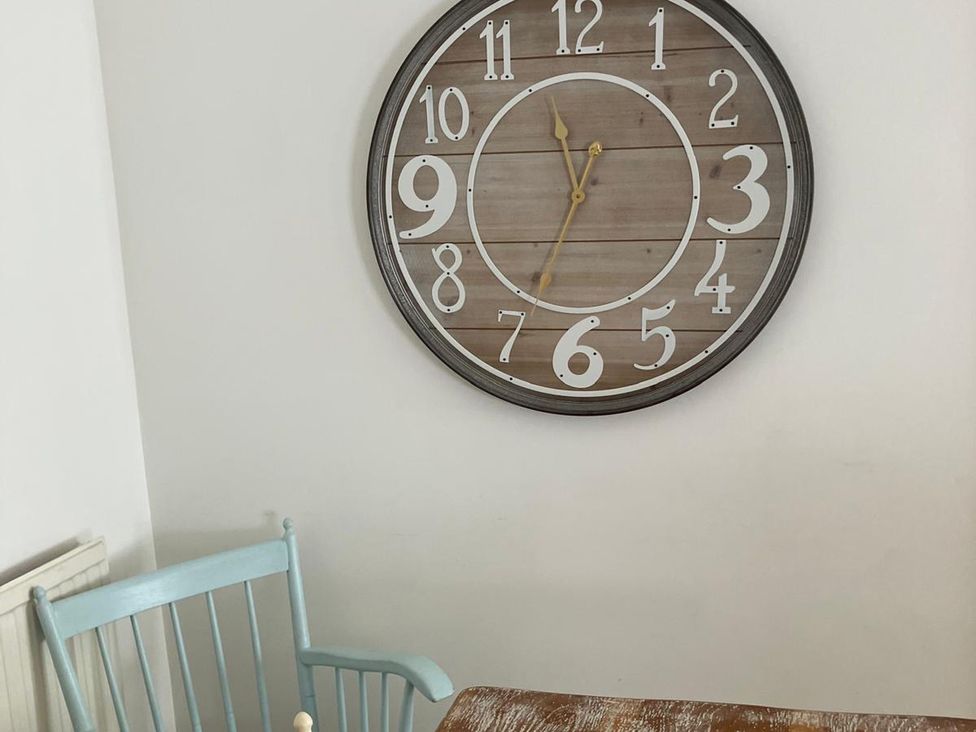 A clock on the wall and a chair beside a table at Claire Cottage