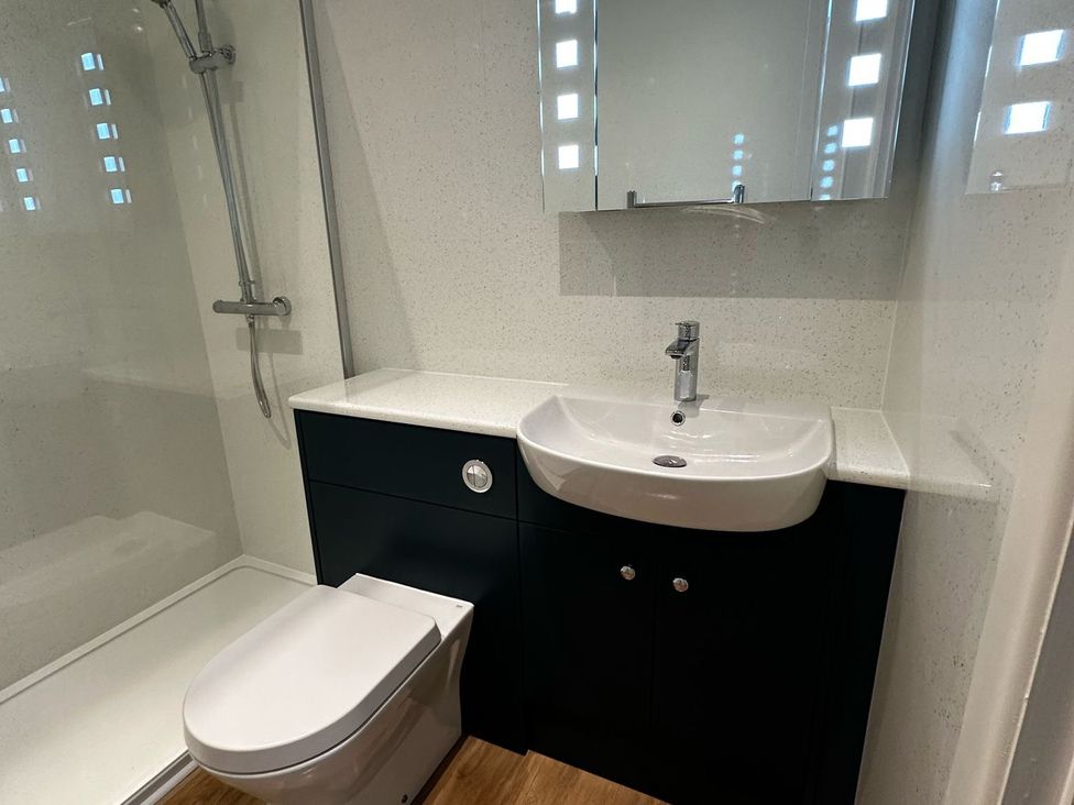 A bathroom with a shower, toilet, sink, and mirror at Claire Cottage