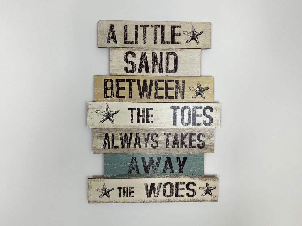 A decorative wooden sign with a quote about sand between toes at Claire Cottage