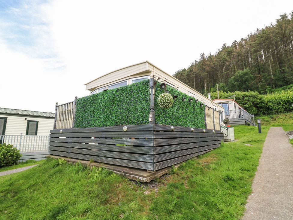 A mobile home with artificial green hedge fencing on a raised deck near a wooded area at GM18 in Clarach Bay near Aberystwyth