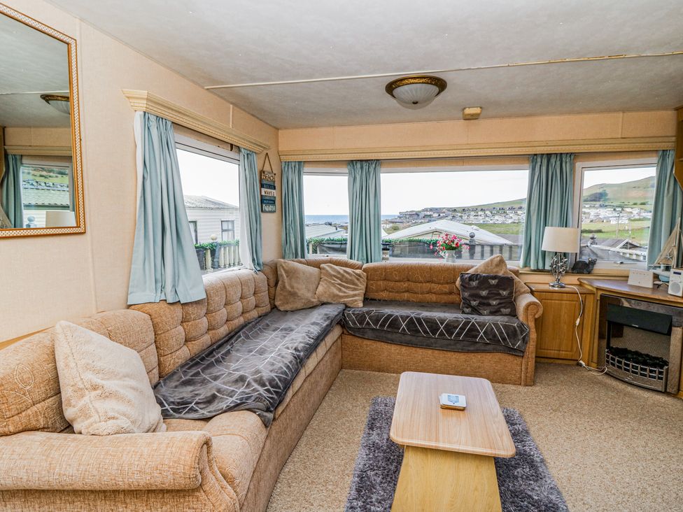 A living room with beige sofas blue curtains a wooden coffee table and a fireplace at GM18 Clarach Bay near Aberystwyth