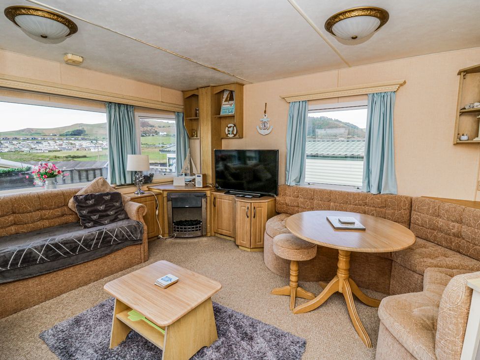 A living room with sofas a round wooden table a small wooden coffee table a television and windows with blue curtains at GM18 Clarach Bay near Aberystwyth