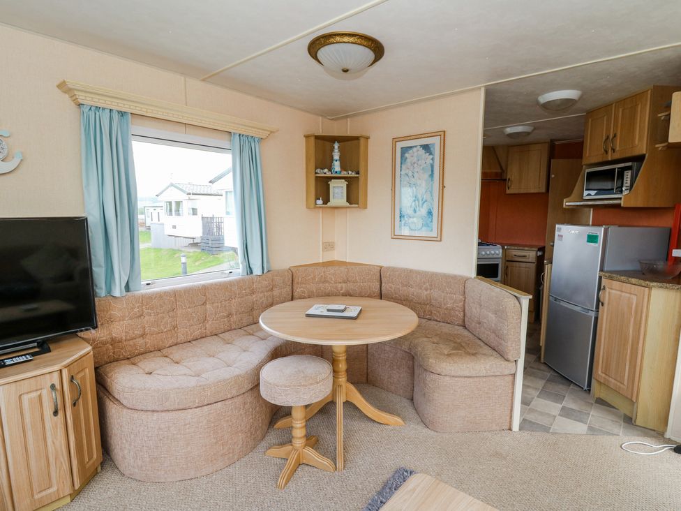 A living area with a corner sofa a round table a stool a television and a kitchen with wooden cabinets at GM18 Clarach Bay near Aberystwyth
