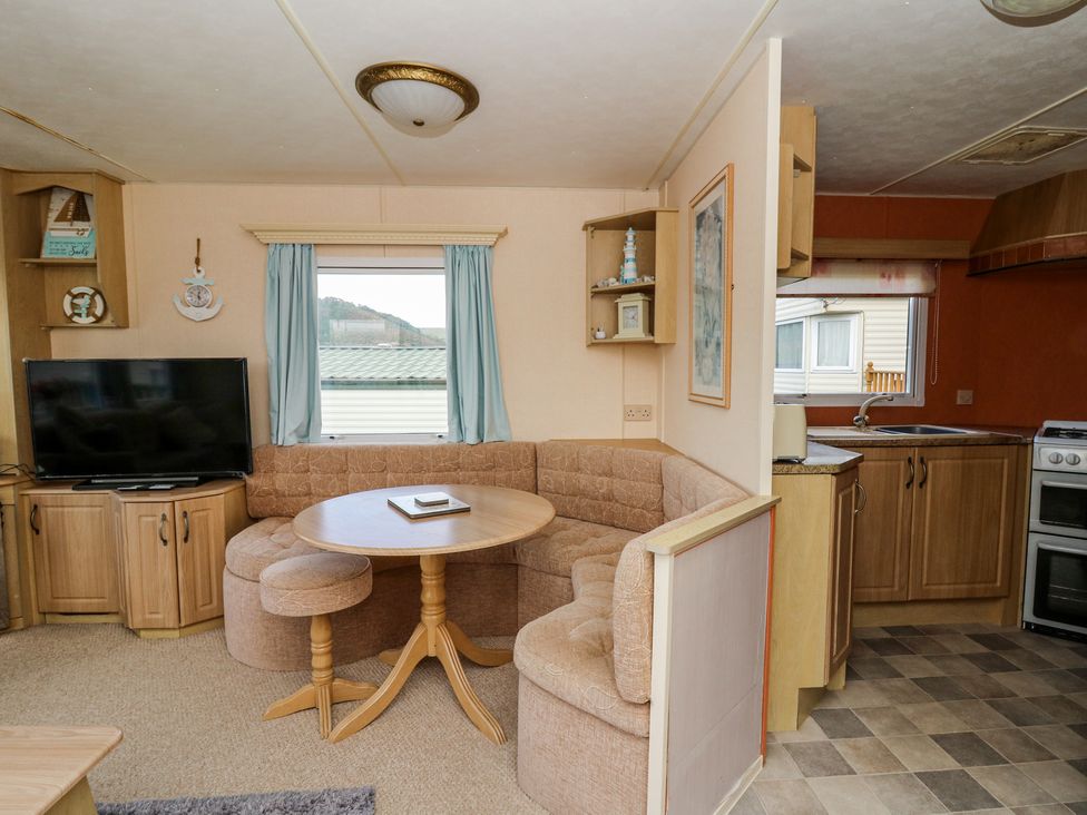 A living area with a round wooden table and curved sofa next to a television and an open kitchen at GM18 in Clarach Bay near Aberystwyth