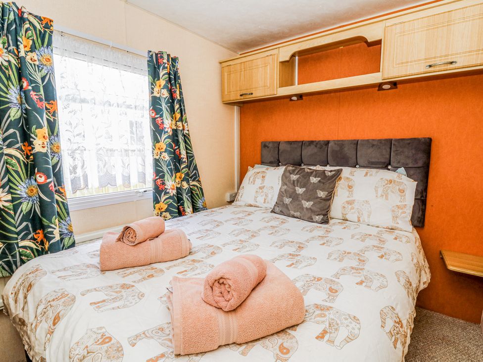 A bedroom with a bed with patterned bedding and folded towels near a window with floral curtains at GM18 in Clarach Bay near Aberystwyth