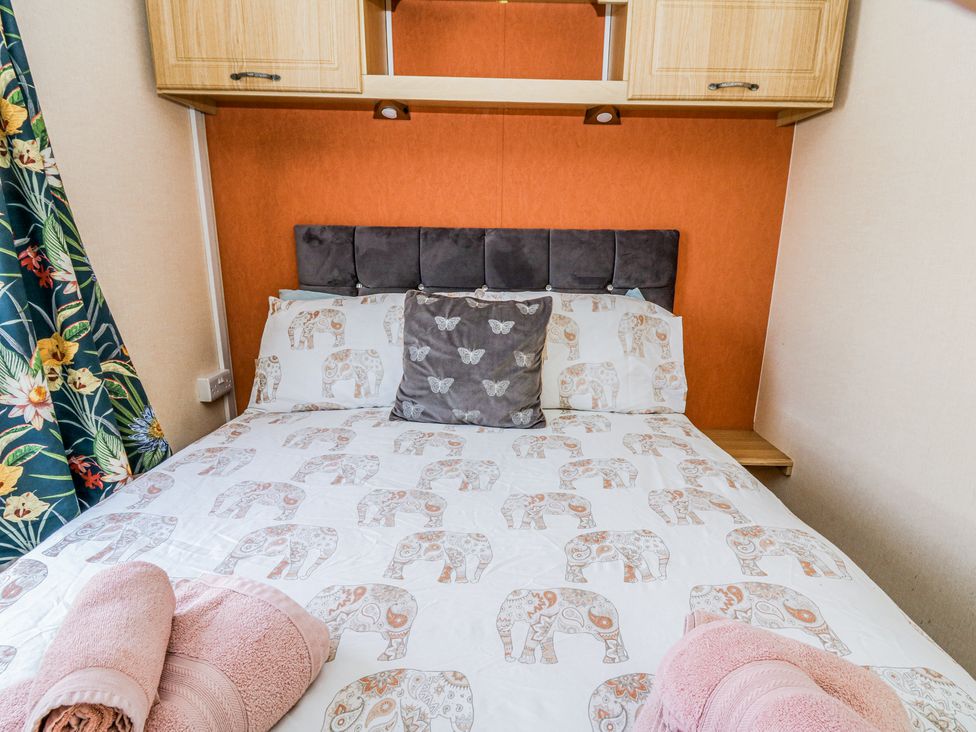 A bedroom with a bed covered in elephant patterned bedding and folded towels at GM18 Clarach Bay near Aberystwyth