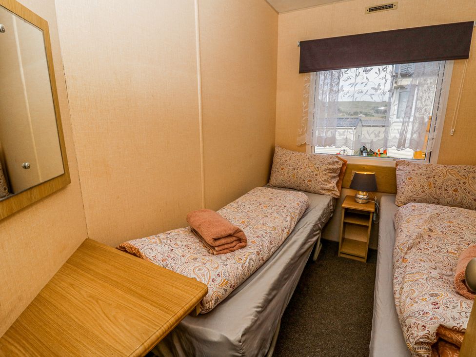 A small bedroom with two single beds bedside table lamp and a window with blinds at GM18 Clarach Bay near Aberystwyth