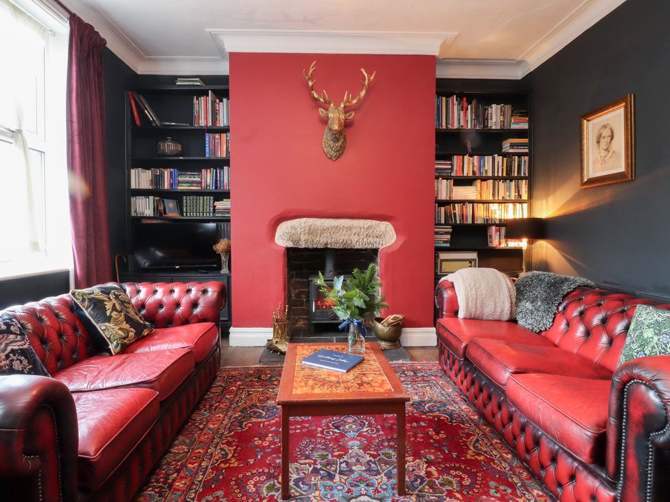 A living room with red sofas and bookshelves at Heathcliff Cottage