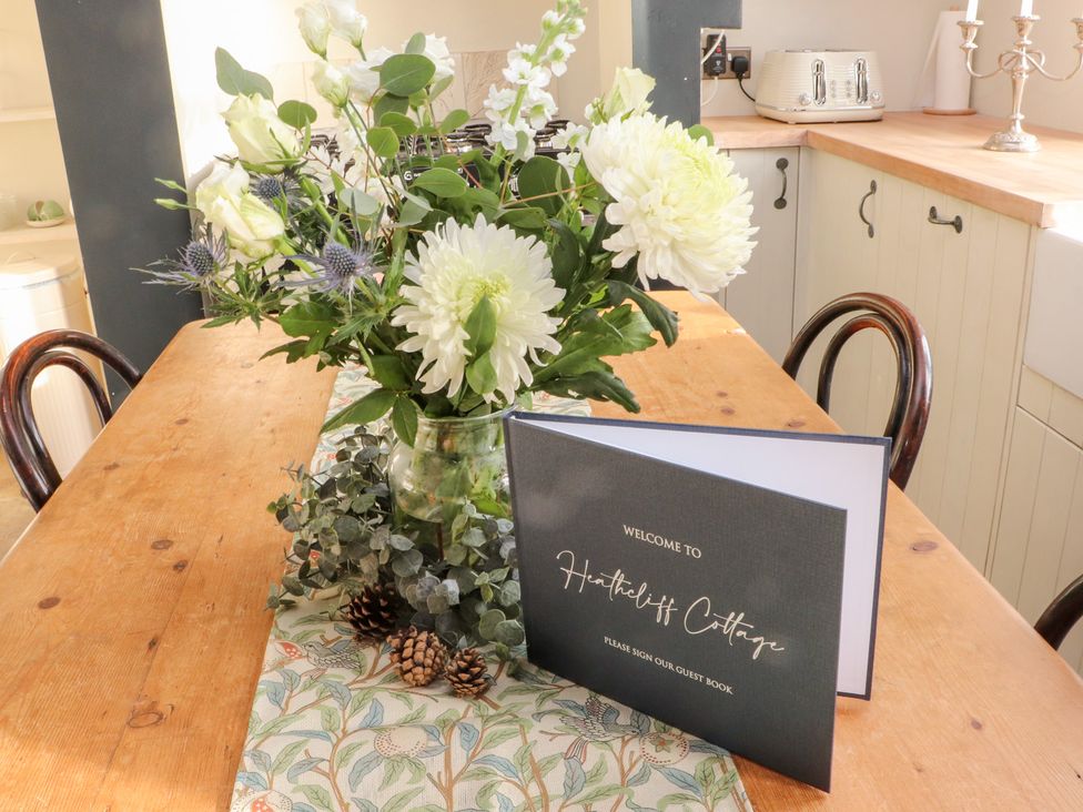 A kitchen table with a flower vase and guest book at Heathcliff Cottage